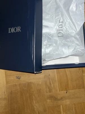 Vita Dior sneakers med reflekterande detaljer - Säljer ett par vita Dior sneakers med reflekterande detaljer och snygg, futuristisk design. Skorna har en chunky sula, mesh och syntetmaterial samt tydliga Dior-loggor på plösen och sidan. Perfekta för dig som vill sticka ut med exklusiva sneakers.