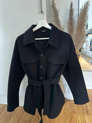 Kappa från ginatricot  - Sparsamt använd kappa från ginatricot. Köpt 2023 och har jättefint skick. Bandet runt midjan går att ta bort. 