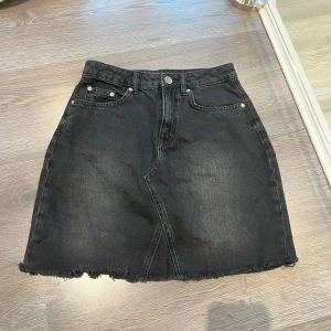 Svart jeanskjol från HM, 32 - Snygg svart jeanskjol från HM (Divided). Kjolen har knapp och dragkedja framtill samt bälteshällor. Säljer då den är för liten för mig💖