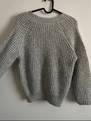 Grå chunky stickad tröja - Mysig grå stickad tröja med grov struktur och rund hals. Tröjan har långa ärmar och ribbade muddar vid ärmslut och nederkant. Perfekt för kalla dagar och enkel att matcha med jeans eller kjol. 