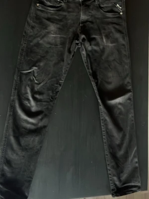 Svarta Replay jeans slim fit - Säljer ett par svarta jeans från Replay i modellen Anbass. Jeansen har slim fit passform, klassisk femficksdesign och är tillverkade i stretchigt denimtyg för extra komfort. Snygga detaljer med Replay-logga på fickan och knapp.