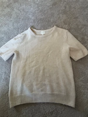 Beige stickad t-shirt från H&M - Kortärmad stickad t-shirt i beige från H&M. Tröjan har rund halsringning, ribbade muddar vid ärmslut och nederkant samt en mjuk och enkel design. Perfekt för lager på lager och en clean look.Skriv privat för mer bilder❤️