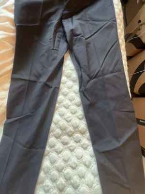 Mörkgrå kostymbyxor från Sand - Snygga mörkgrå kostymbyxor från Sand Copenhagen med klassisk rak passform och pressveck. Tillverkade i ett tunt, elegant tyg som ger en stilren look. Perfekta för dig som vill ha en clean och dressad stil.