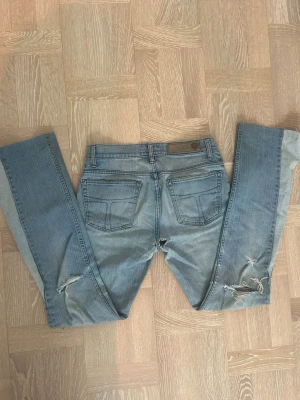 Ljusblå Tiger of Sweden jeans bootcut - Säljer ett par ljusblå jeans från Tiger of Sweden med bootcut-modell och slitna detaljer på benen. De har ett hål i skrevet men går säkert att sy igen! Klassisk femficksdesign. Perfekta för dig som gillar en avslappnad och trendig look.
