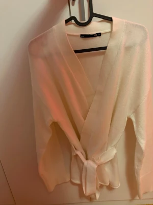 Vit kofta  - Snygg vit tkofta med knytband i midjan och långa ärmar. Koftan har en mjuk och tunn stickning som ger en clean och stilren look. Perfekt att slänga över en topp för en chill vibe.