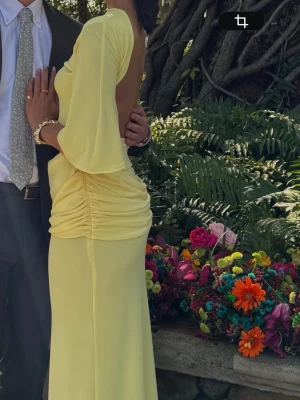 Ljusgul långklänning med öppen rygg från Zara - Trendig ljusgul långklänning från Zara med öppen rygg och slits i sidan samt ett band om sidan. Sålde slut direkt i höstas när den kom! Klänningen har vida ärmar och rynkade detaljer vid höften vilket ger en väldigt fin siluett. Använd vid ett tillfälle och aldrig fått så mycket komplimanger förut för en klänning. Jag har sytt upp rynkningen för att dölja undertyget vilket jag tycker blev mycket bättre. Bild 2,3 är lånade. Se bild 4 & 6 för att se rynkningen :)