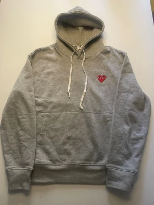Grå Comme des Garçons Play hoodie - Säljer denna sjukt snygga hoodie från cdg. Tröjan är i mycket bra skick och är enkel och matcha till. Storlek m, personen på bilden är ca 180. Skriv vid minst funderingar!