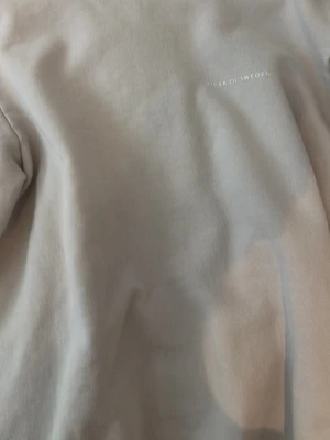 Beige hoodie från Tiger of Sweden - Snygg beige hoodie från Tiger of Sweden med diskret logga på bröstet. Tillverkad i mjukt och skönt material med borstad insida för extra komfort. Klassisk passform och ribbade muddar vid ärmslut och nederkant. Perfekt för en clean och stilren look.