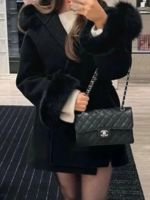 Svart kappa med fuskpälsdetaljer - Stilren svart kappa med stora fuskpälsdetaljer vid huva och ärmslut. Kappan har en rak passform och knälång längd, perfekt för en trendig look. Bär den över en stickad tröja för extra värme och stil.one size.