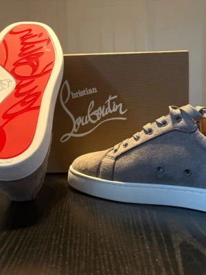 Gråa Christian Louboutin  - Snygga gråa sneakers från Christian Louboutin i mocka med klassisk röd sula och vita kanter. Skorna har lågt skaft, rund tå och matchande grå skosnören. Perfekta skor till sommaren, kan gå ner i pris kom privat!