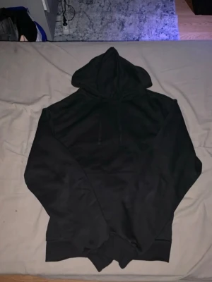 Svart hoodie med huva - En klassisk svart hoodie med huva och dragsnören. Hoodien har en avslappnad passform och ribbade muddar vid ärmslut och nederkant. Perfekt för en chill och stilren look.