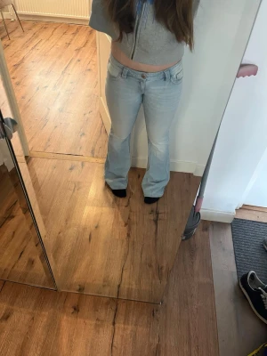 Ljusblå bootcut jeans med låg midja - Säljer ett par ljusblå bootcut jeans med låg midja och klassiska fem fickor. Jeansen har snygga detaljer på bakfickorna och är i ett mjukt denimtyg. Perfekta för en avslappnad och trendig look.