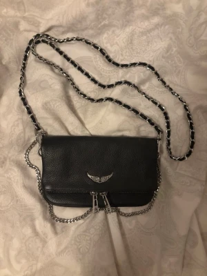 Svart Zadig & Voltaire axelväska - Cool svart axelväska i läder från Zadig & Voltaire med silverfärgad kedjerem och detaljer. Väskan har dubbla dragkedjor framtill. Perfekt för dig som gillar snygga accessoarer. 
