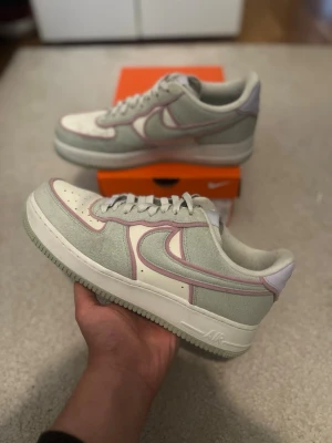 Nike Air Force 1 - Nike Air Force 1 Sage sneakers i ljusgrönt mocka och vitt läder med lila detaljer runt swoosh och paneler. Klassisk låg siluett med perforerad tåbox och vit sula. Perfekta för dig som gillar stilrena men unika sneakers.