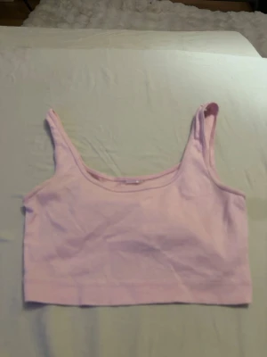 Ljusrosa kort ribbad linnetopp - Söt ljusrosa kort croppad linnetopp med breda axelband och ribbad struktur. Perfekt till sommaren och enkel att matcha med jeans eller kjol. Mjuk och stretchig känsla för en bekväm passform. Säljer för jag inte använder och vet inte riktigt vart den är ifrån eftersom lappen är borta
