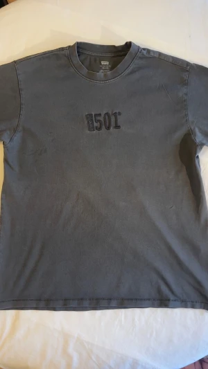 Grå Levi's 501 t-shirt - Säljer en grå t-shirt från Levi's med '501' broderat på bröstet. Klassisk passform med korta ärmar och rund halsringning. Perfekt för dig som gillar enkel och stilren streetwear.