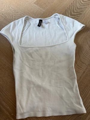 Vit topp med fyrkantig hals från H&M - Säljer en vit topp från H&M med snygg fyrkantig halsringning och korta ärmar. Toppens passform är slim och den är gjord i mjuk bomull, perfekt för att matcha med jeans eller kjol. Enkel och stilren design som är lätt att bära. Skriv för fler bilder. Pris går att diskutera!❤️