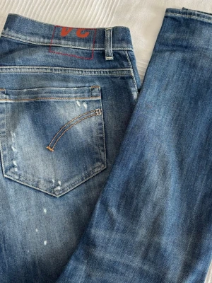 Dondup - George - Säljer ett par blå skinny jeans från George med slitningar och blekta detaljer. Jeansen har klassisk femficksdesign, orange sömmar och VC-märke på bakfickan. Perfekt för dig som gillar en cool och avslappnad look.