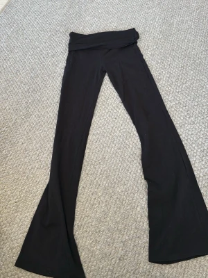Svarta bootcut leggings med vikbar midja - Säljer ett par svarta leggings med bootcut och vikbar midja. De är tillverkade i ett mjukt och stretchigt material som sitter skönt och följer kroppen. Perfekta för en avslappnad och trendig look.