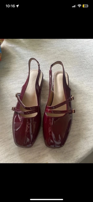 Vinröda lackballerinaskor med remmar - Snygga vinröda ballerinaskor från Topshop i glansigt lackmaterial. Skorna har två smala remmar över foten och en öppen häl med slingback-design. Fyrkantig tå och låg sula ger en modern look. Perfekta för dig som vill ha något stilrent och trendigt.