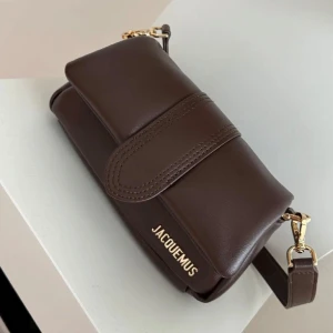 JACQUEMUS VÄSKA  - Intressekoll! Axelremsväska i modellen The Small Bambimou Brown Bag, mini puffed flap leather bag. Dustbag och box medföljer med. Dubbelband tillkommer, justerbar lång och en kort. Inte använd under åren, bara legat i boxen så väskan är princip i nyskick. Finns för upphämtning i Stockholm området.