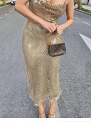 Ny Glittrig guldig långklänning Zara  - Säljer en glittrig långklänning i guld med tunna axelband och snygg draperad urringning. Klänningen har ett tätt paljettmönster som ger en riktigt festlig look. Perfekt för dig som vill sticka ut och glänsa på nästa event! Helt ny och slutsåld från Zara viral och populär modell