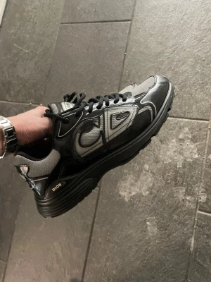 B30 - Snygga b30 i svart och grått med tydliga logodetaljer på sidan och sulan. Skorna har en chunky sula, svarta skosnören och meshpaneler kombinerat med läderdetaljer för en modern och sportig look.