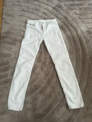 Vita jeans från DSQAURED2 - Snygga vita skinny jeans från DSQAURED2 med klassisk femficksdesign och läderpatch med logga bak i midjan. Jeansen har låg midja och smal passform, perfekta för en trendig look. Tillverkade i bomull med lite stretch för extra komfort.