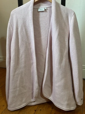 Ljusrosa kofta från Boomerang - Ljusrosa stickad kofta från Boomerang i storlek L. Koftan har öppen front utan knappar, mjuk struktur och diskret Boomerang-logga på ärmen. Perfekt för lager-på-lager och enkel att matcha med olika outfits.