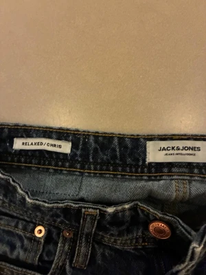 Blå relaxed jeans Jack & Jones - Säljer ett par blå relaxed fit jeans från Jack & Jones, modell Chris. Klassisk femficksdesign med kopparfärgade nitar och kontrastsömmar. Perfekta för en avslappnad stil och tillverkade i slitstarkt denimtyg. Använd ett par gånger.