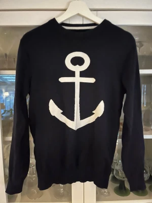 Marinblå stickad tröja Clean Cut - Snygg marinblå stickad tröja från Clean Cut Copenhagen i storlek XS. Tröjan har ett stort vitt ankare på bröstet och ribbstickad rund hals. Hör av dig vid intresse eller minsta fråga.