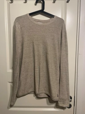 Beige långärmad tröja i mjukt material - En stilren beige långärmad tröja med rund halsringning. Tröjan är tillverkad i ett mjukt och tunt stickat material som ger en avslappnad och enkel look. Perfekt för lager-på-lager och passar till det mesta i garderoben.