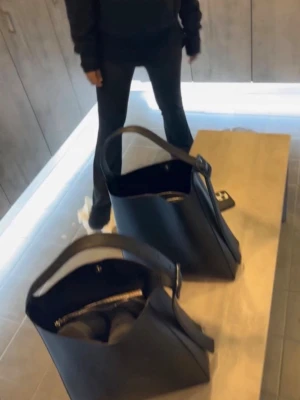 Svart bucket bag i läderlook - Begagnad Axelväska med ett fack med dragkedja samt knapp i mitten av väskan. Väskan är begagnad med i mycket god skick. Använt kanske under en månads period och fungerar precis som en helt ny väska 