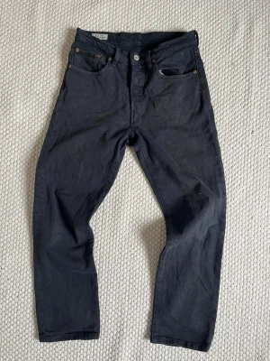 Levi’s 501 - Snygga svarta jeans från Levi's med klassisk femficksmodell och raka ben. Jeansen har knappgylf och detaljer i kopparfärgad metall. Tillverkade i bomull med en stilren look och diskret läderpatch bak i midjan.