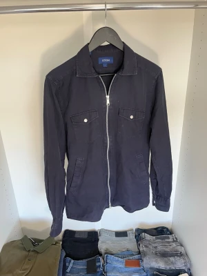Mörkblå overshirt från Eton - Snygg mörkblå overshirt från Eton med dragkedja framtill, två bröstfickor med lock och knappar samt två sidfickor. Overshirten har klassisk krage och raka ärmslut. Hör gärna av dig vid frågor!