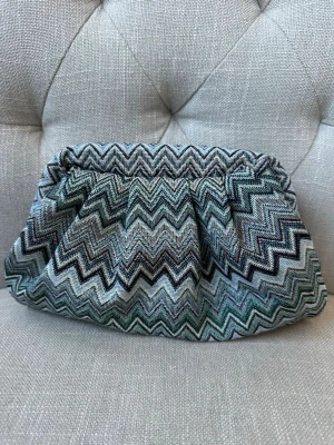 Clutchväska med zigzag-mönster - Snygg kuvertväska i tyg med zigzag-mönster. Väskan har en mjuk form och stängs med metallspänne. Insidan är fodrad i ljusgrönt tyg. Perfekt accessoar för att lyfta din outfit. Väskan är handgjord