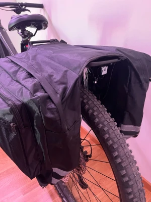 Svart cykelväska med dubbla sidofack - Säljer en svart cykelväska med två stora sidofack som enkelt hängs över pakethållaren. Väskan är tillverkad i slitstark textil och har dragkedjor för smidig förvaring. Perfekt för dig som vill ha extra utrymme på cykelturen.