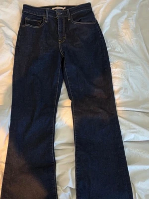 Mörkblå bootcut jeans från Levi's - Snygga mörkblå jeans från Levi's med bootcut passform och klassiska kontrastsömmar. Jeansen har fem fickor, hällor för bälte och en läderpatch bak i midjan. Tillverkade i kraftig denim med en tidlös look.