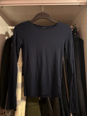Mörkblå långärmad topp från Gina Tricot - En enkel och stilren mörkblå långärmad topp från Gina Tricot. Modellen har rund halsringning och är gjord i mjuk bomull som känns skön mot huden. Perfekt att matcha med jeans eller kjol för en clean look.