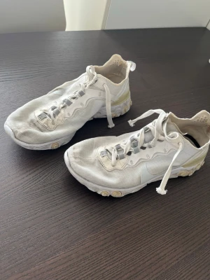 Nike React Element 87 vita sneakers - Nike React Element 87 sneakers i vitt med genomskinliga meshpaneler och detaljer i grått och beige. Skorna har en unik sula med runda gummipluppar och vågiga linjer längs ovandelen. Lätta och luftiga med snörning och låg profil.