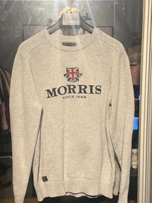Grå tröja från Morris med tryck - Snygg grå tröja från Morris med broderad logga och brittisk flagga på bröstet. Rund halsringning och ribbade muddar vid ärmslut och nederkant. Perfekt för en stilren och avslappnad look.