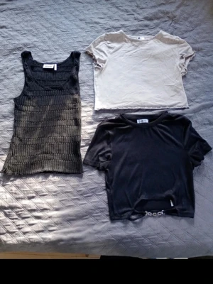 Tre trendiga toppar i svart och beige - Säljer tre snygga toppar: en ribbad svart linnetopp, en croppad beige t-shirt och en svart croppad t-shirt med kedjedetalj. Perfekta för att mixa och matcha till olika outfits. Passar dig som gillar en modern och avslappnad stil. Alla i M ☺️