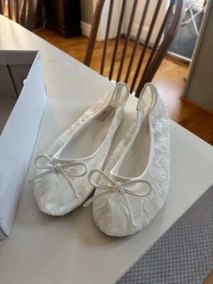 Vita spetsballerinaskor från Nelly - Snygga vita ballerinaskor från Nelly med spetsdetaljer och rosett framtill. De är endast använda en gång. De är i jättebra skick och är endast smutsiga undertill. Kan vara lite stor i storleken.