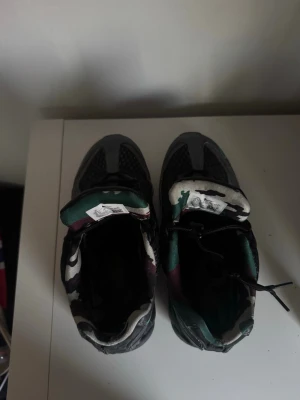 Svarta sneakers med camomönster Nike X corteiz - Säljer ett par svarta sneakers med coolt camomönster i grönt, vitt och svart på plösen och insidan. Skorna har en chunky sula och meshdetaljer på ovandelen för extra ventilation. Perfekta för dig som vill sticka ut med din stil. Lite trasiga men säljes för rätt pris 
