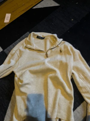 Beige halvzip tröja från Polo Ralph Lauren - Snygg beige långärmad tröja från Polo Ralph Lauren med halvzip och liten broderad logga på bröstet. Tröjan har hög krage och är tillverkad i mjukt material, perfekt för lager på lager. Enkel och stilren design som passar till det mesta.