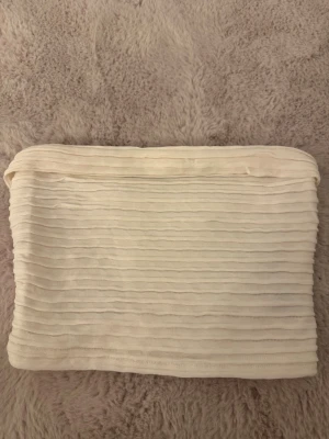 Vit ribbad bandeau tubtopp - Säljer en vit bandeau tubtopp med ribbade detaljer. Toppen är axelbandslös och har en stretchig passform som sitter snyggt på kroppen. Perfekt att matcha med höga jeans eller kjol för en trendig look.