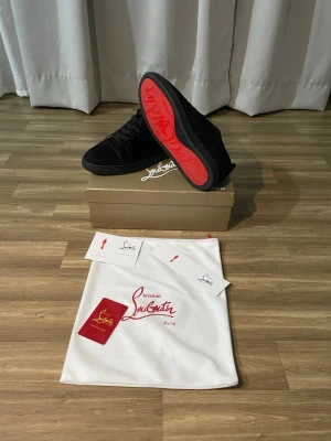 Svarta skor frånChristian Louboutin - Stilrena svarta sneakers i mocka från Christian Louboutin med den ikoniska röda sulan och diskreta detaljer. Lågt skaft och svarta skosnören ger en clean look. Perfekta för dig som vill ha något exklusivt och trendigt.