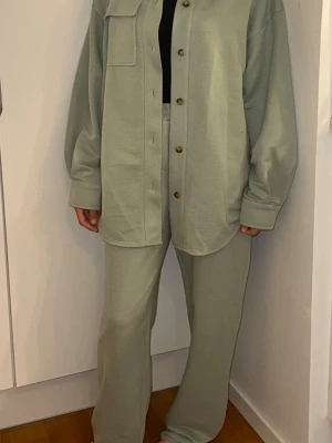 Ljusgröna 2 - 2 del outfit. Mjukisbyxor och en matchande kofta i ljusgrön färg med rak passform och hög midja byxor . Tillverkade i ett mjukt och stretchigt material som känns riktigt skönt. Perfekta för en avslappnad stil. Mjukisbyxorna är flera gånger använda men fortfarande i fint skick. Lite noppor finns, men de är knappt märkbara när byxorna används. OBS! Modellen är XS och bär en S vara