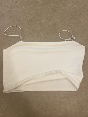 Vit linnetopp från Bebe - Säljer en enkel och stilren vit linnetopp från Bebe med tunna axelband. Toppen har en croppad passform och är tillverkad i ett mjukt material som känns skönt mot huden. Perfekt att matcha med jeans eller kjol för en fräsch look.