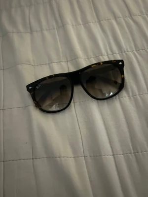 Ray-Ban  solglasögon - Snygga Ray-Ban Wayfarer solglasögon med svart och sköldpaddsmönstrad båge. Glasen är tonade i brunt och har en klassisk fyrkantig form. Perfekta för dig som vill ha en tidlös och trendig accessoar till sommaren. Nästan helt nya och har inga repor eller annat. 